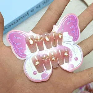 Detalle en primer plano de uñas postizas degradadas con perlas y finas líneas doradas.