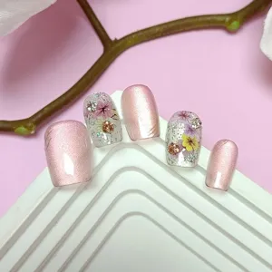 Primer plano detallado de uñas postizas cortas hechas a mano de ojo de gato rosa con flores secas.