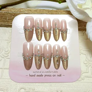Uñas postizas artesanales con diseño cat-eye francés dorado, base nude y pedrería de brillantes finos.