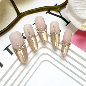 Vista detallada de uñas postizas cat-eye hechas a mano con borde dorado francés y pedrería.