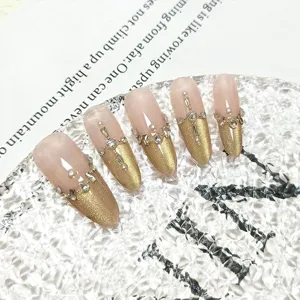 Detalle de uñas postizas hechas a mano, degradado cat-eye dorado con perlas y pedrería brillante.