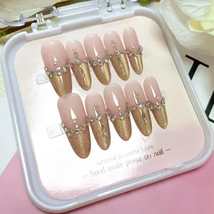 Detalle de uñas postizas almendradas hechas a mano, ojo de gato dorado con perlas estrás.