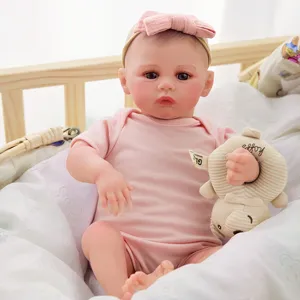 Gros plan détail du poupon reborn de 20 pouces tenant un petit ours dans un lit confortable.