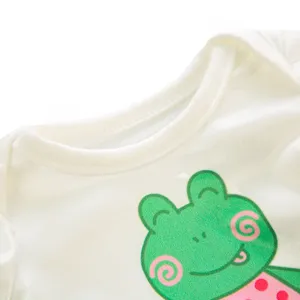 Weißes Puppenkleidung Detailbild mit grünem Cartoon Frosch Motiv auf weichem weißem Stoff.