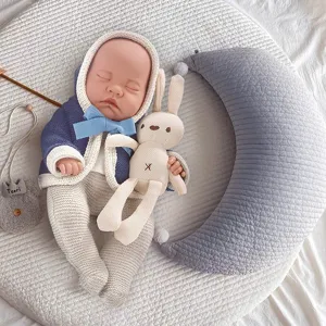 Detailed view of 12-inch reborn baby doll with knitted outfit and bunny toy in cozy setup.