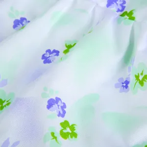 Nahaufnahme des Puppenkleidstoffes mit Blumenmuster, lila Blüten auf weißem Hintergrund.