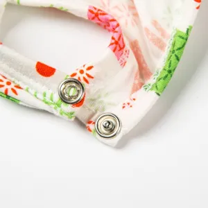Close-up detail of doll clothes featuring colorful floral print fabric and metal snap buttons.