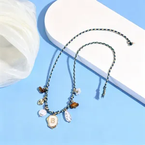 Detailed view of bohemian braided anklet with letter charm, pearl and shell, beach jewelry.