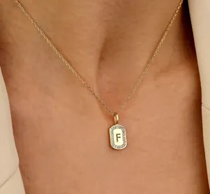 Detailopname van de gouden ketting met een rechthoekige hanger met zirkonia en letter F.