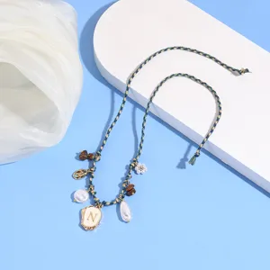 Boho braided anklet detail featuring letter N pendant, pearls and shell charms for beach summer.