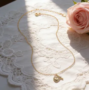 Detailed shot of a delicate gold clavicle chain featuring a rhinestone heart lock and key pendant.