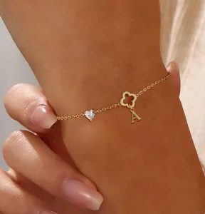 Nahaufnahme Detail der goldfarbenen Kette mit Kleeblatt, Herzanhänger und Buchstabenanhang.