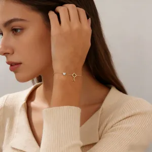 Nahaufnahme eines filigranen goldfarbenen Armbands mit Kleeblatt-Anhänger und Buchstaben.
