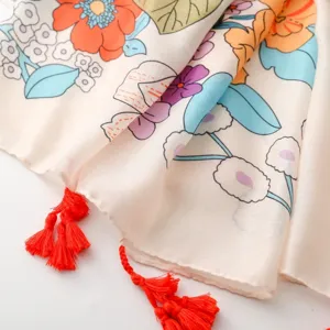 Gros plan détail d'écharpe à imprimé floral ethnique, couleurs vives et franges rouges.