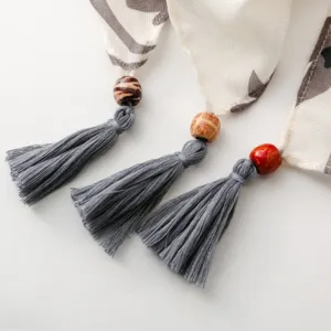 Primo piano dettaglio di foulard stile etnico con nappina e decorazione di perle di legno.