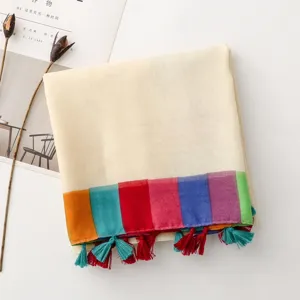 Vue détail d'une écharpe en coton et lin avec bordure arc-en-ciel colorée et glands de plage.