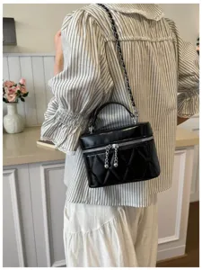 Detalle de un bolso bandolera acolchado negro con cadena en un ambiente de cocina acogedor.