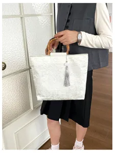 Detailansicht der weißen strukturierten Handtasche mit Bambusgriff und eleganter Quaste.