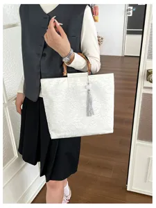 Detail du sac blanc style chinois avec poignees en bambou naturel et pendentif pompon elegant.