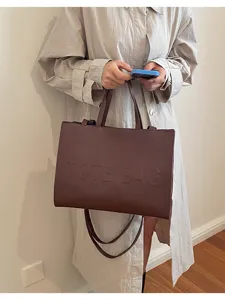 Primer plano de un bolso tote marrón elegante con texto en relieve, ideal para el trabajo.