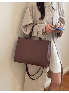 Primer plano detallado del bolso tote marrón elegante con texto en relieve y asas firmes.