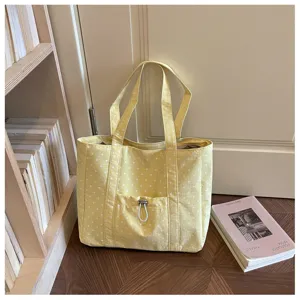 Dettaglio scena di una borsa tote in tela a pois gialli con spallacci e tasca frontale.
