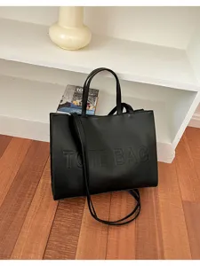 Vista detallada de un bolso tote negro con textura de cuero, gran capacidad y correa.