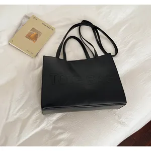 Vista detallada del bolso tote negro con texto en relieve y doble correa para el hombro.