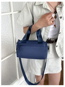 Vista detallada del elegante bolso cilíndrico de nailon azul oscuro llevado por la modelo.