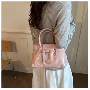 Pink patent leather handbag detail shot showing chic front belt buckle design and dual top handles.