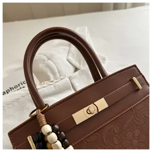 Detalle de bolso de mano marrón con cierre de giro metálico y abalorio de cuentas decorativo.