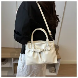 Detail shot of a white patent leather shoulder bag featuring a chic belt buckle and handle.