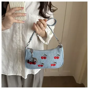 Detailed view of a light blue denim shoulder bag with red cherry embroidery and charm.