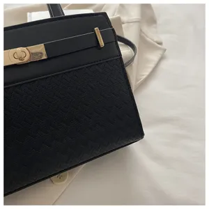 Detailopname van de elegante zwarte handtas met getextureerd geweven patroon en goud hardware.