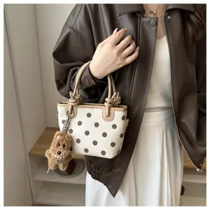 Gros plan du sac seau à pois beige avec poignées nouées et joli pendentif chiot mignon.