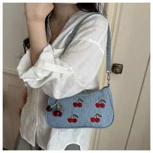 Blue denim shoulder bag with red cherry embroidery and charm for women daily use.