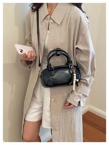 Vista detallada de un elegante bolso de mano cilíndrico de charol negro con colgante de cuentas.
