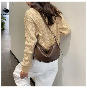 Vista dettagliata di borsa a spalla a mezzaluna in pelle marrone indossata da modella.
