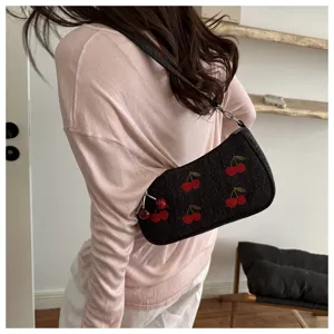 Detailed view of dark denim shoulder bag with cute red embroidered cherry patterns and charm.