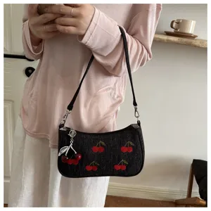 Close-up of vintage dark denim shoulder bag with red cherry embroidery and chic metal charm.