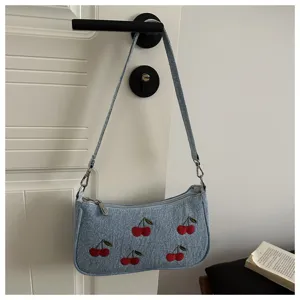 Detailed view of a light blue denim shoulder bag featuring cute embroidered red cherries.