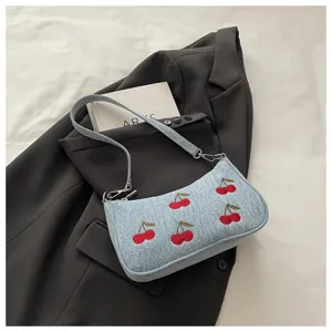 Detailed view of trendy denim shoulder bag featuring cute red cherry embroidery and hardware.