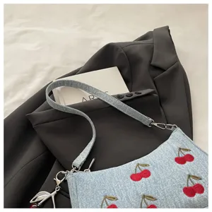 Close-up detail of the vintage cherry embroidered denim shoulder bag, styled with fashion props.