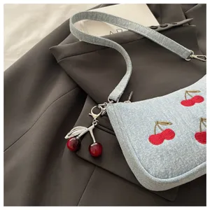 Light blue denim shoulder bag featuring red cherry embroidery and chic metal charm.