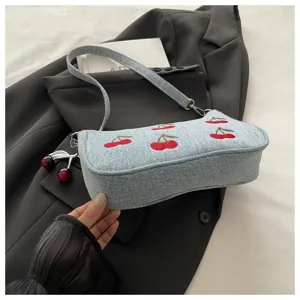 Close-up detail of vintage denim shoulder bag with red cherry embroidery and lovely charm.