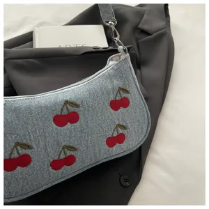Close-up view of the chic denim shoulder bag featuring cute embroidered red cherry patterns and metal hardware.