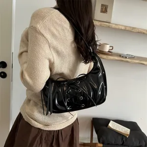 Élégant sac à bandoulière noir en cuir verni avec design plissé chic et jolis détails de laçage.