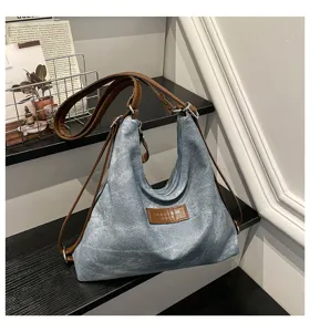 Dettaglio borsa shopper in denim con cinturini in pelle marrone e etichetta frontale. Casual.