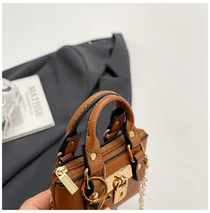 Detalle de bolso bandolera mini marrón, cuero texturizado y herrajes metálicos dorados.