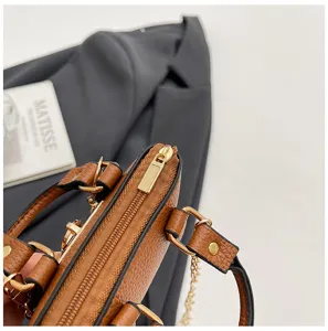 Detalle de bolso cruzado de cuero texturizado marrón con cremallera dorada y accesorios.